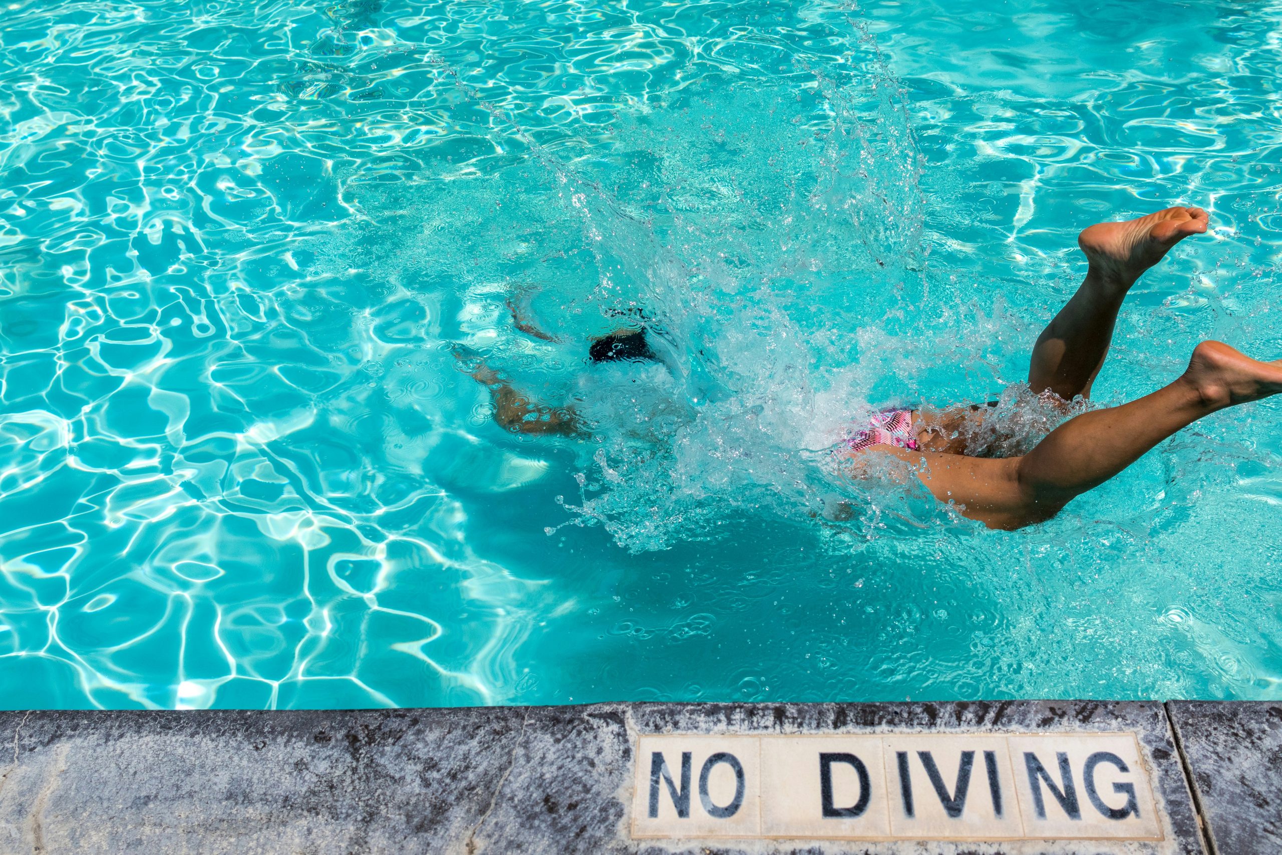 a person diving into a swimming pool next to a "no diving" sign